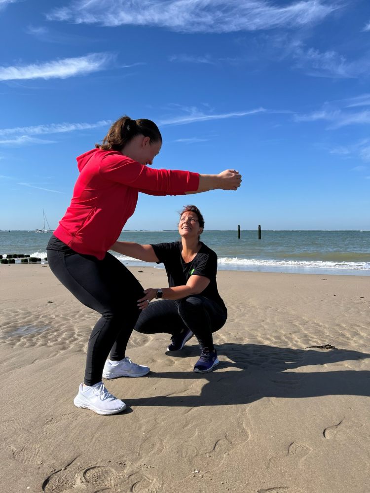 Sandy begeleidt een cliënt bij een squat op het strand